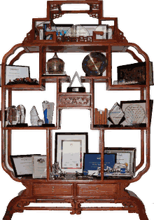 A carved wooden display shelf holding trophies, plaques and framed certificates