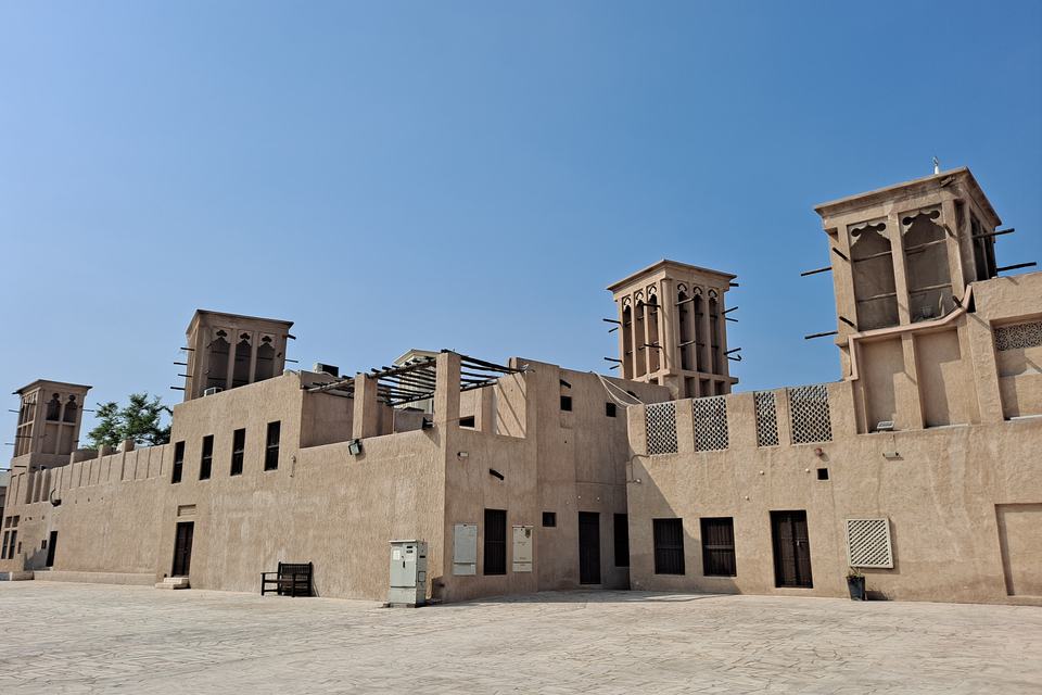 Four wind towers rising above the sand-coloured traditional houses of Al Fahidi historic quarter in Dubai, under a clear blue sky