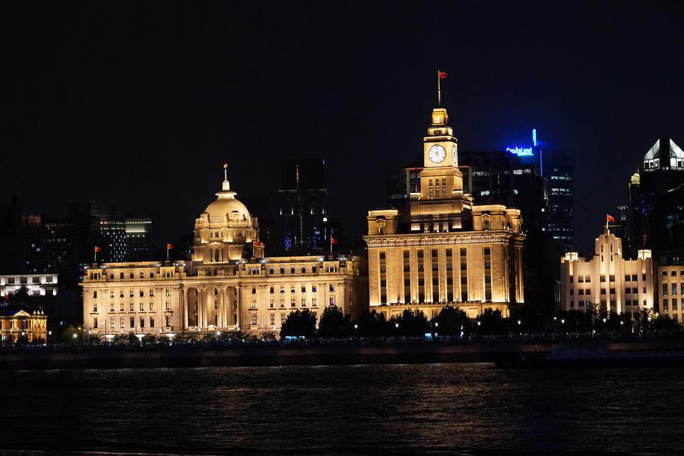 The floodlit Customs House clock tower and the domed former HSBC Building on the Bund in Shanghai, seen across the Huangpu River at night.